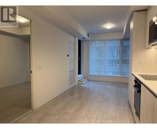 A spacious room with wooden flooring and a kitchen area with white cabinets.