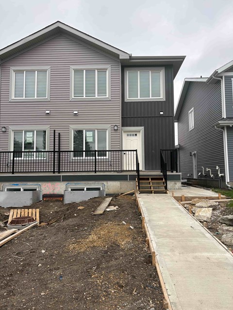 A house under construction with a grey facade and a black fence.