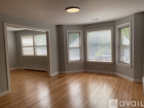 A spacious room with wooden floors and three windows.