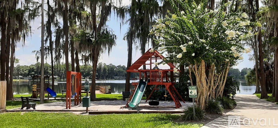 A playground with a red swing set and a green slide is surrounded by trees.