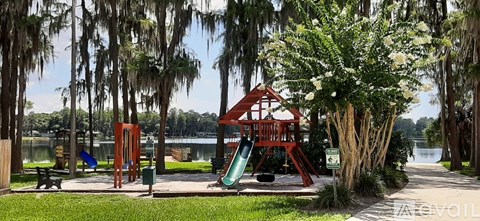 A playground with a red swing set and a green slide is surrounded by trees.