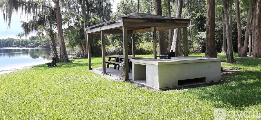 A pavilion with a table and chairs is situated in a grassy area near a lake.