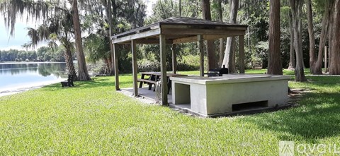 A pavilion with a table and chairs is situated in a grassy area near a lake.