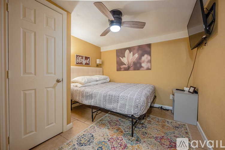 A bedroom with a bed, a ceiling fan, and a television mounted on the wall.