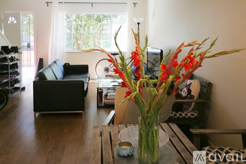 A vase with red flowers sits on a wooden table in a living room.