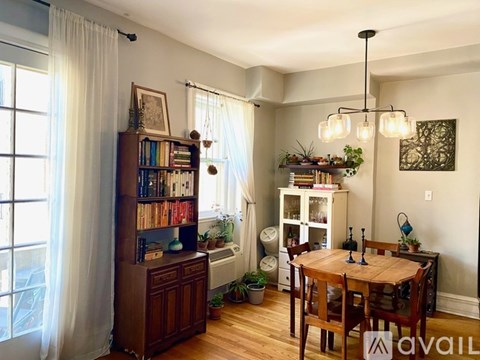 A living room with a wooden table and chairs, a bookcase, and a window with curtains.