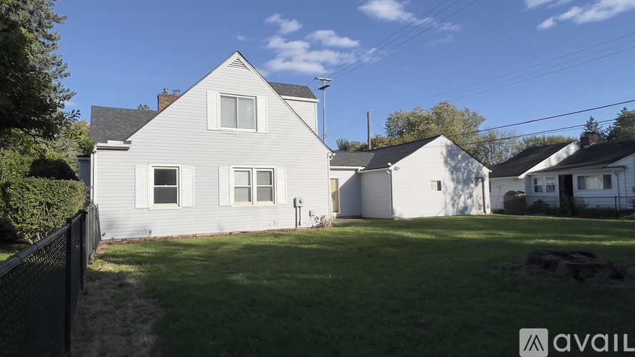 A house with a white exterior and a grey roof is surrounded by a grassy area and other houses.