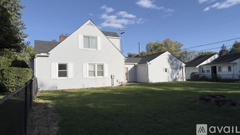 A house with a white exterior and a grey roof is surrounded by a grassy area and other houses.