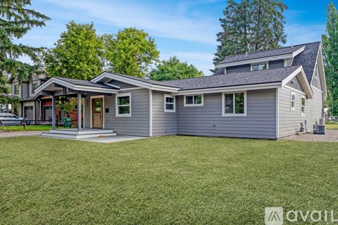 A house with a grey exterior and a red door is surrounded by green grass and trees.