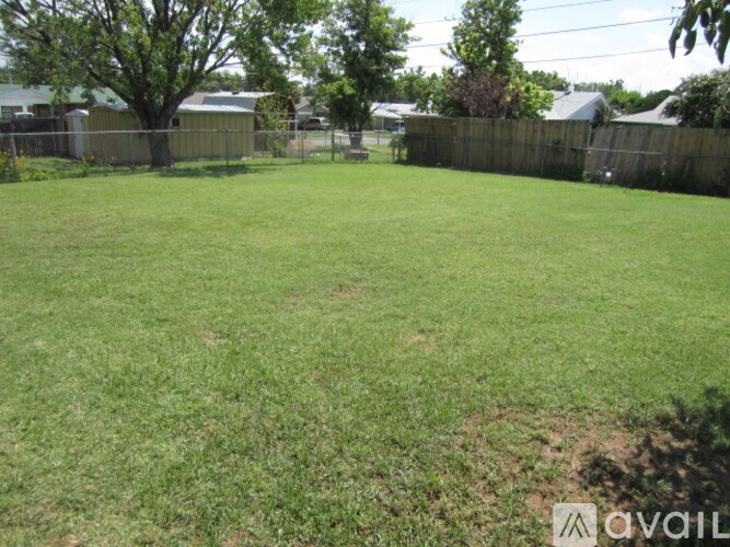 A grassy backyard with a fence and trees.