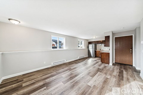 A spacious room with wooden flooring and a kitchen area in the background.