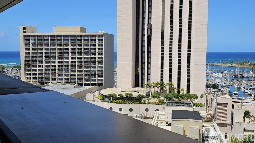 A view of a cityscape with a large building in the foreground and a marina in the background.