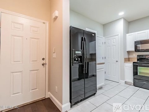 A black fridge in a kitchen with white cabinets and a white door.