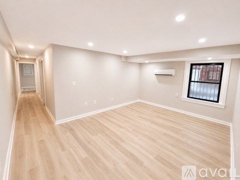 A spacious room with wooden flooring and a window with blinds.