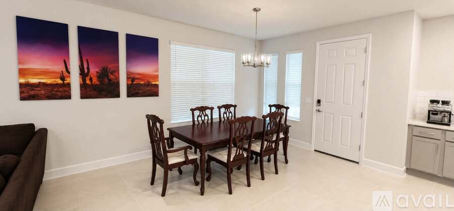 A dining room with a brown table and chairs, a chandelier, and three landscape paintings on the wall.
