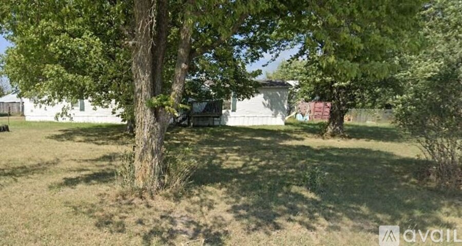 A tree in a grassy field with a house in the background.