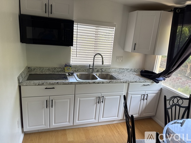 A kitchen with white cabinets and a black microwave above the sink.