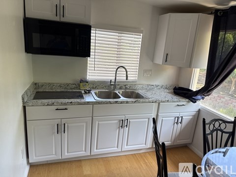 A kitchen with white cabinets and a black microwave above the sink.