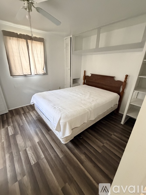 A bedroom with a bed, wooden flooring, and a window with curtains.