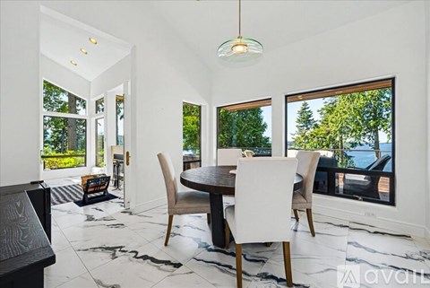 A dining room with a table and chairs and a view of trees outside the window.