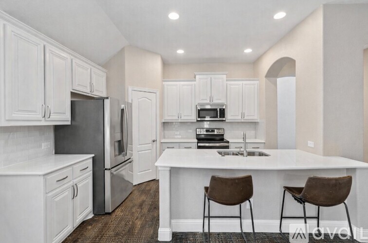 A kitchen with white cabinets and a white island with two brown chairs.