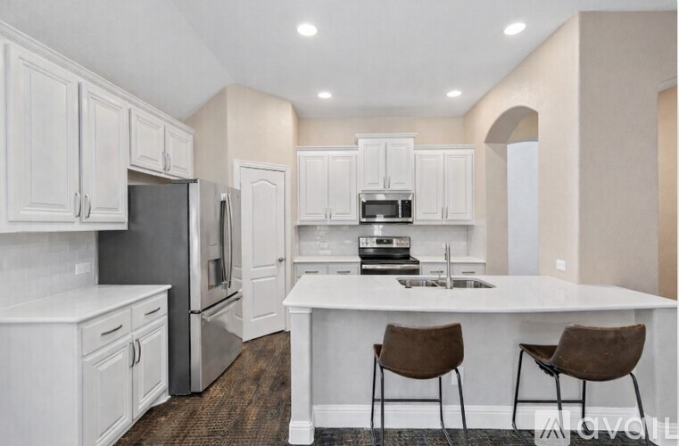 A kitchen with white cabinets and a white island with two brown chairs.
