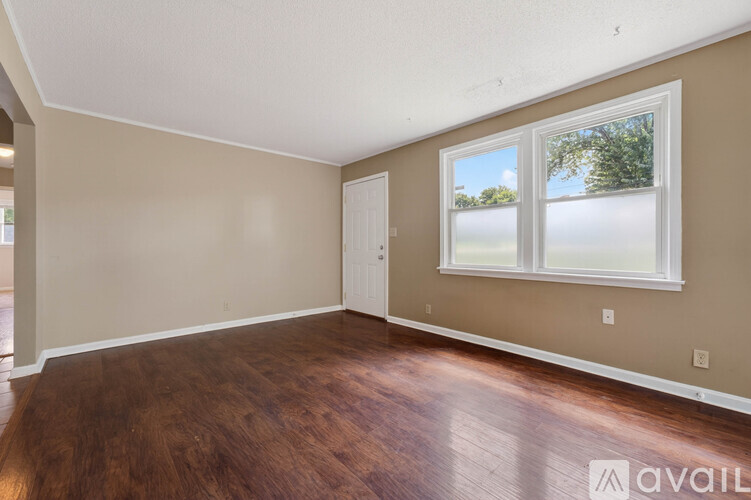 A room with a brown floor and a window showing the sky and trees outside.