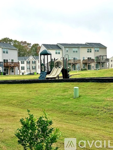 A playground with a slide in the middle of a grassy area in front of apartment buildings.