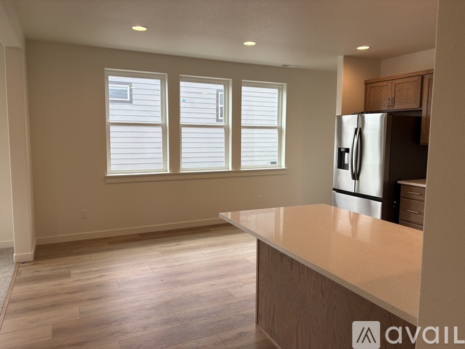 A kitchen with a refrigerator, wooden floors, and a window with blinds.