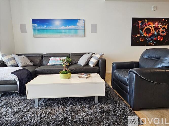 A living room with a large painting on the wall and a black leather couch.