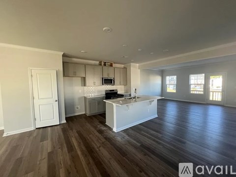 A spacious room with wooden floors and a kitchen area with white cabinets and appliances.