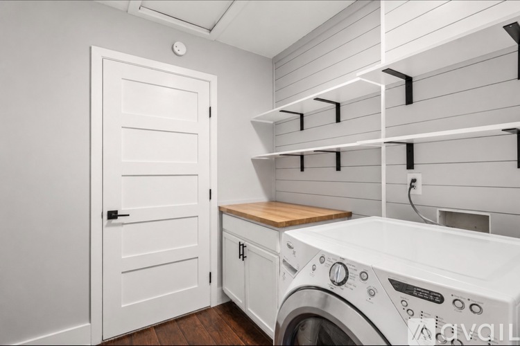 A washing machine is in a laundry room with a door and shelves.