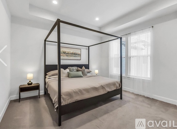 A bedroom with a four poster bed, a nightstand with a lamp, and a painting on the wall.