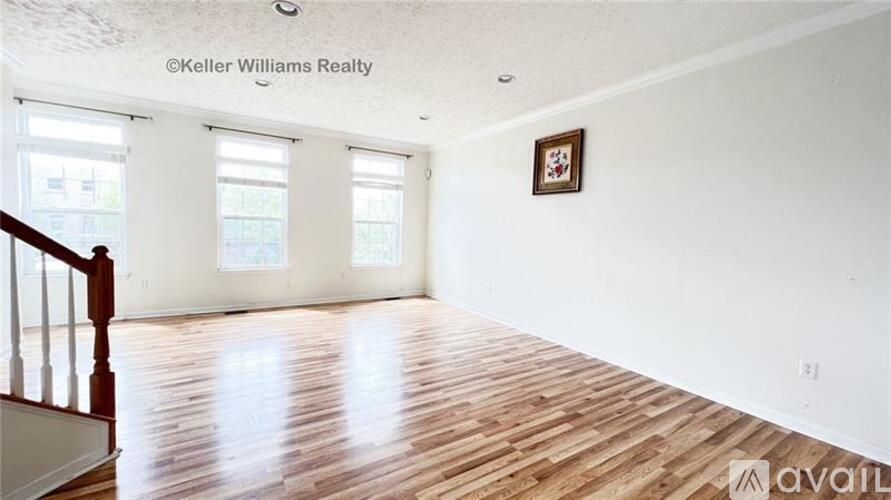 A room with wooden floors and white walls, with a window and a picture on the wall.