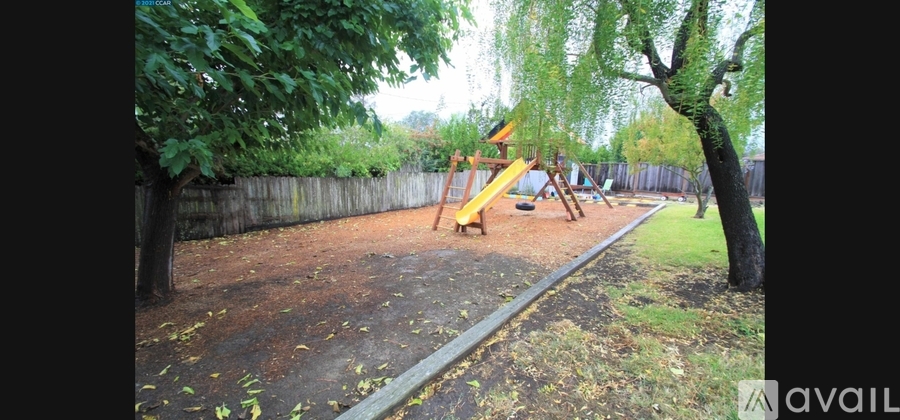 A playground with a yellow slide and a red swing set.