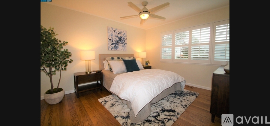 A bedroom with a bed, a ceiling fan, and a potted plant.