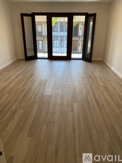 A room with wooden flooring and a large window with a view of a balcony.