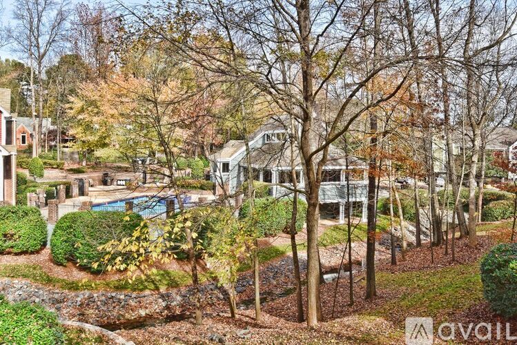 A view of a tree-lined street with a house and a pool in the background.