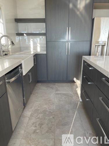 A kitchen with a white counter top and a dog walking through it.