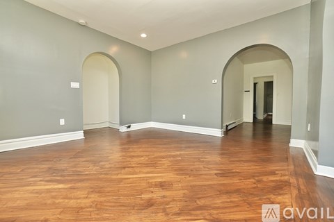 A spacious room with wooden floors and arched doorways.