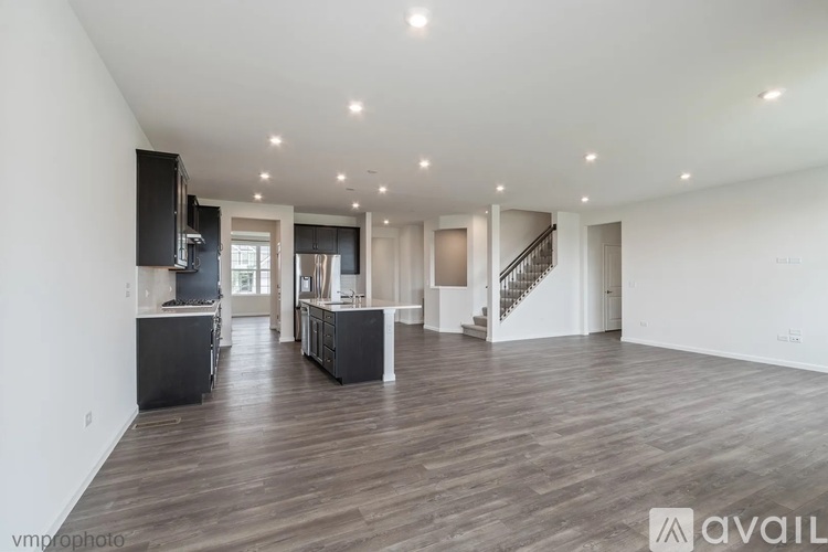 A spacious living room with wooden flooring and a staircase in the background.