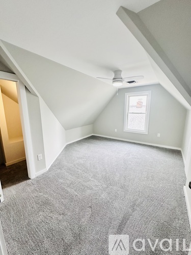 A spacious attic room with a window and carpeted floor.