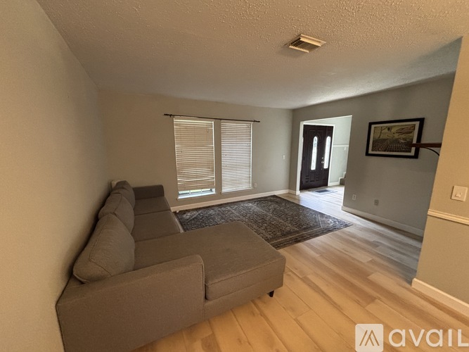 A living room with a grey couch and a rug in front of a window.