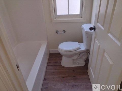 A white toilet in a small bathroom with wooden floors and a window.