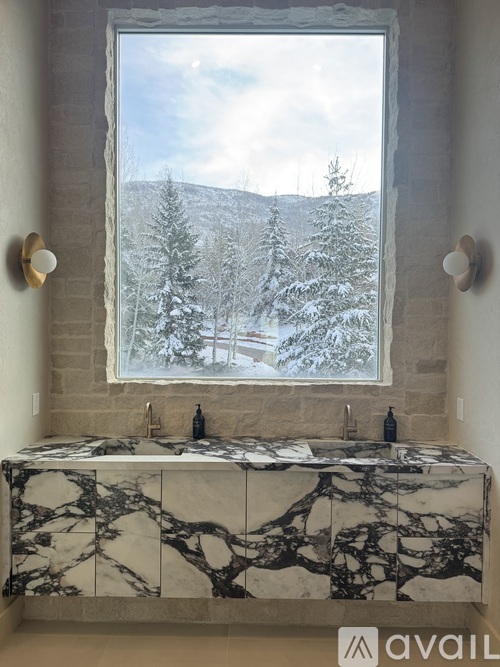 A bathroom with a marble countertop and a window overlooking a snowy landscape.