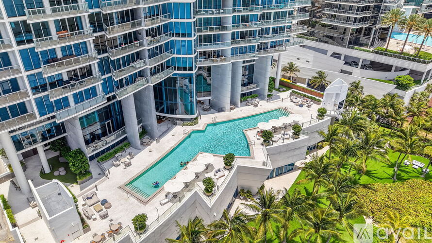 A large pool surrounded by palm trees and a white building with blue balconies.