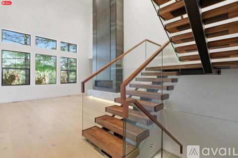 A wooden staircase with glass railings leads up to a balcony with a view of trees.