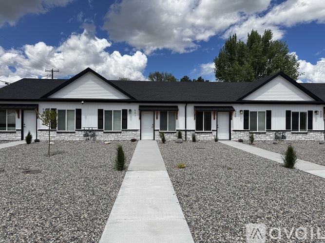 A white house with a black roof and a gravel driveway.