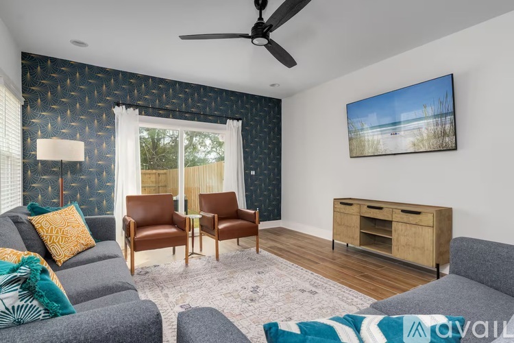 A living room with a grey couch, two chairs, a TV, and a painting of a beach scene on the wall.