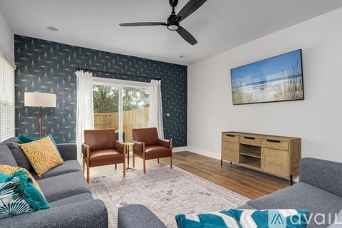 A living room with a grey couch, two chairs, a TV, and a painting of a beach scene on the wall.